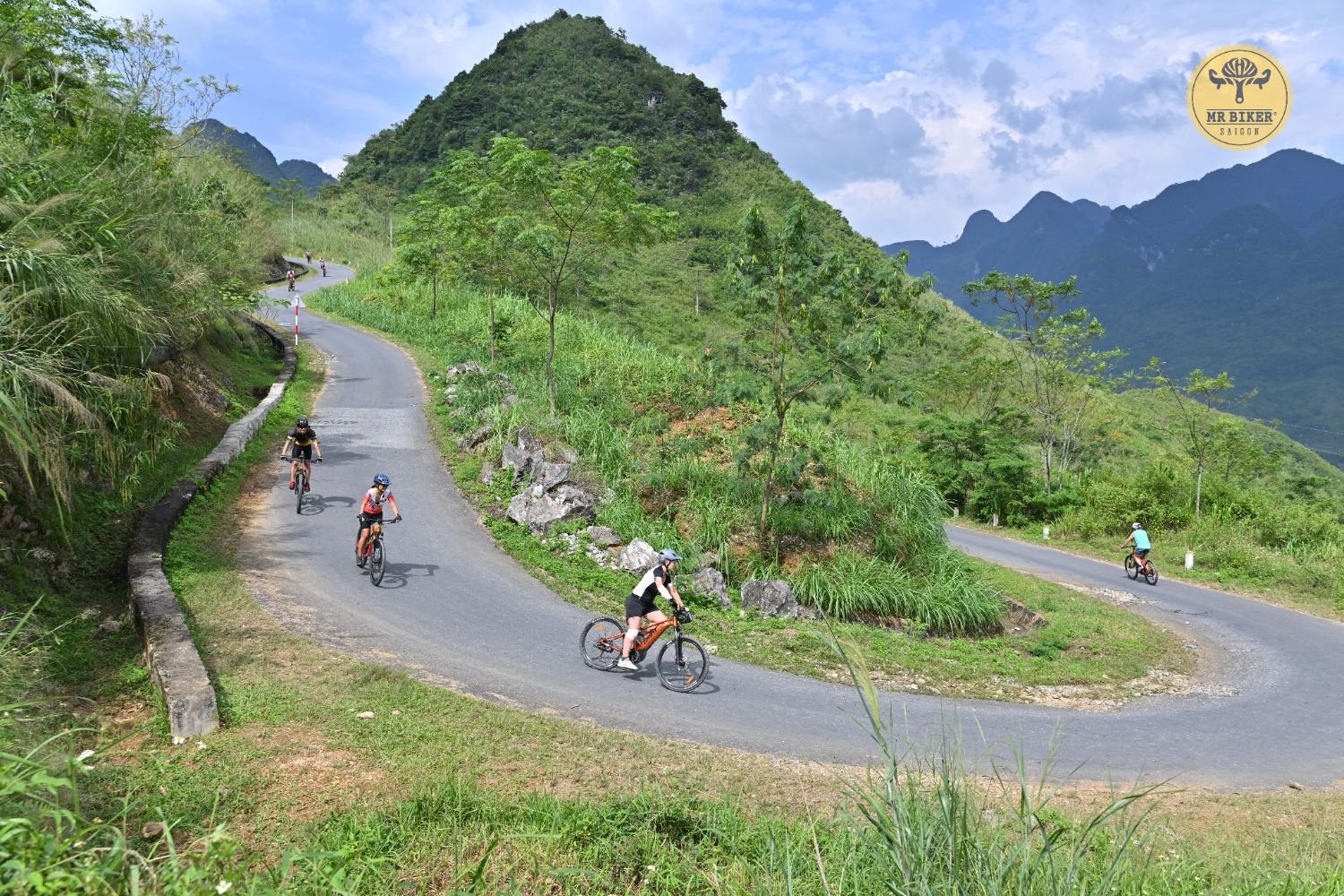 Cyclists riding a switchback mountain road through Ha Giang's karst terrain