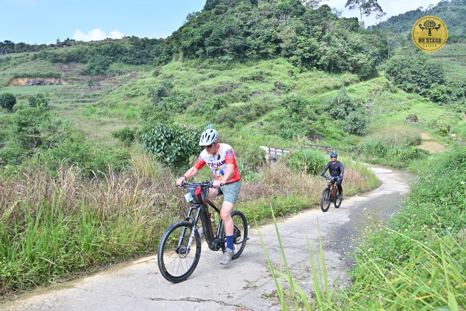 A cyclist rides an e-bike along a quiet village road through the hills near Meo Vac, Ha Giang