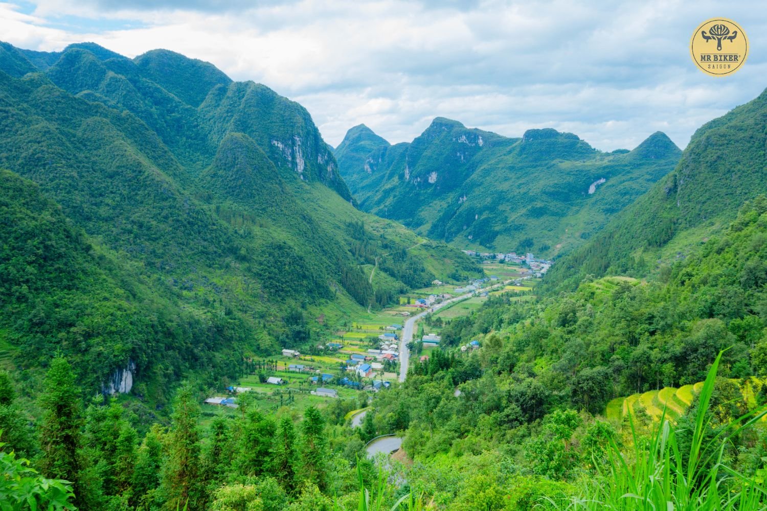 A quiet mountain road winding down into a village valley surrounded by karst peaks in Ha Giang, Vietnam