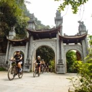 Cyclists riding through an ancient stone gate on a Vietnam cycling tour