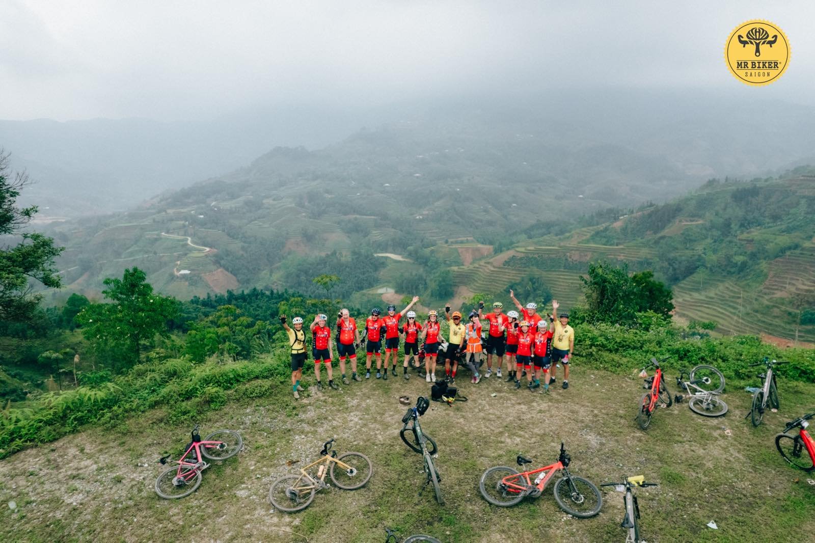Cycling tour group celebrating at a mountain summit overlooking Vietnam's rice terraces